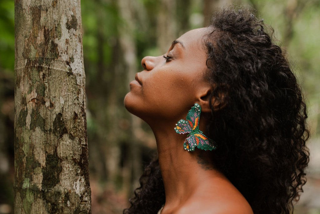 Woman with butterfly earrings standing next to a tree in a forest